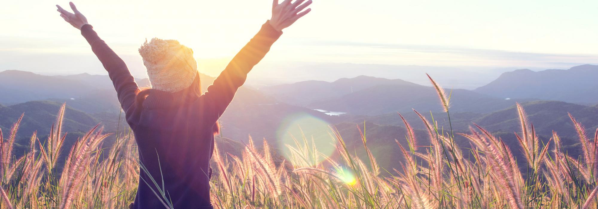 Woman with arms up looking into distance over eastern mountains